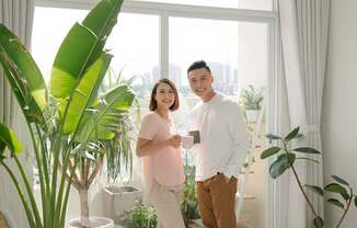 A man and woman standing in a room with a large window and plants.