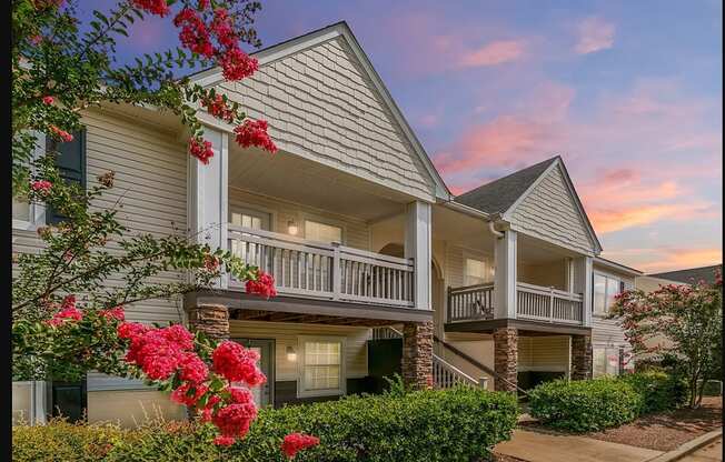A building with a balcony and a tree with red flowers in front.