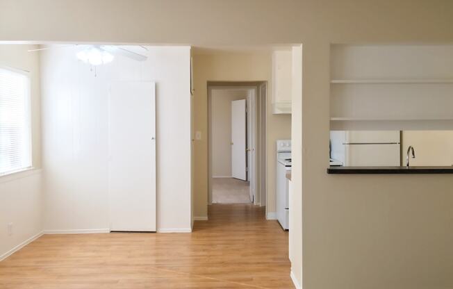 an empty living room with a hard wood floor and a hallway to a kitchen