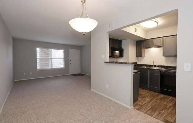 an empty living room with a kitchen in the background