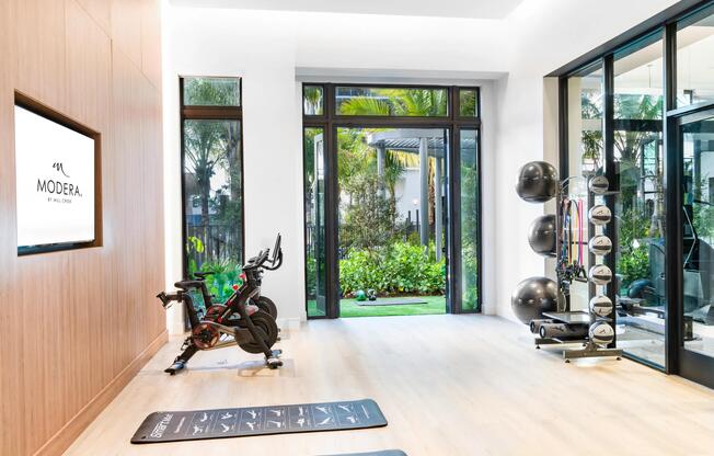 A light-filled fitness studio at Modera Aventura, designed with warm wood tones and direct garden access for an indoor-outdoor workout experience.