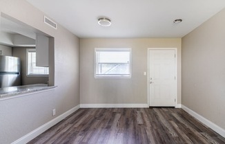 an empty living room with wood flooring and a door to the kitchen