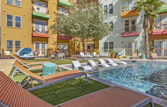 a pool with lounge chairs and a tree in front of a building