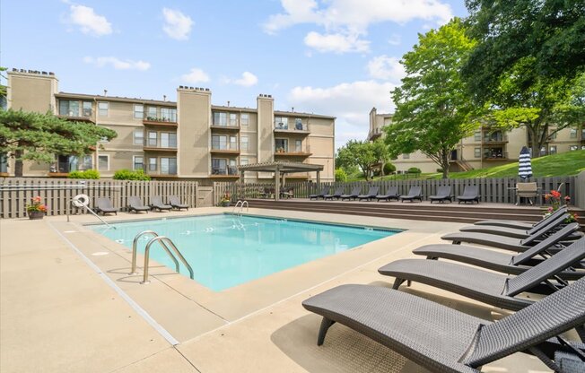 A pool surrounded by lounge chairs and trees.