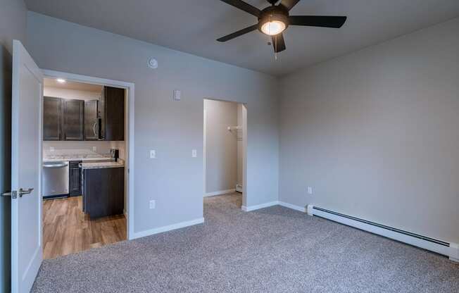 a bedroom with a ceiling fan and a kitchen. Fargo, ND Prairiewood Meadows Apartments