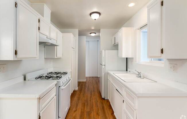 A white kitchen with wood floors and white appliances.