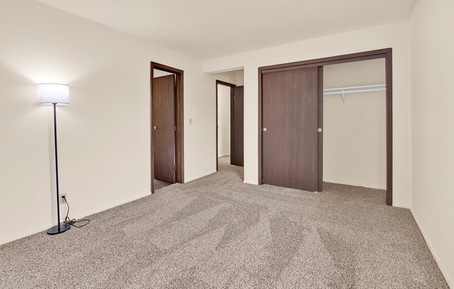 A carpeted room with a lamp and two doors.