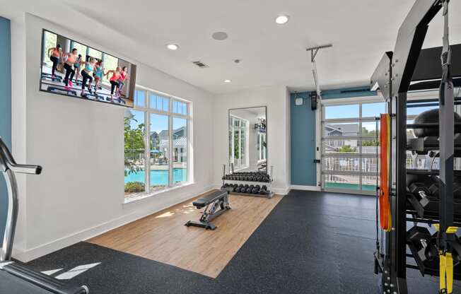 a gym with weights and a tv on the wall and a view of a pool