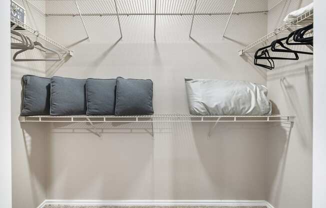 a walk in closet with white walls and shelves and a closet organizer with pillows
