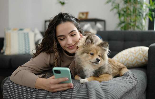 a woman laying on a couch holding a dog and looking at her cell phone
