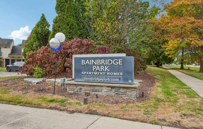 A sign for Bainbridge Park Apartment Homes is in front of a tree.