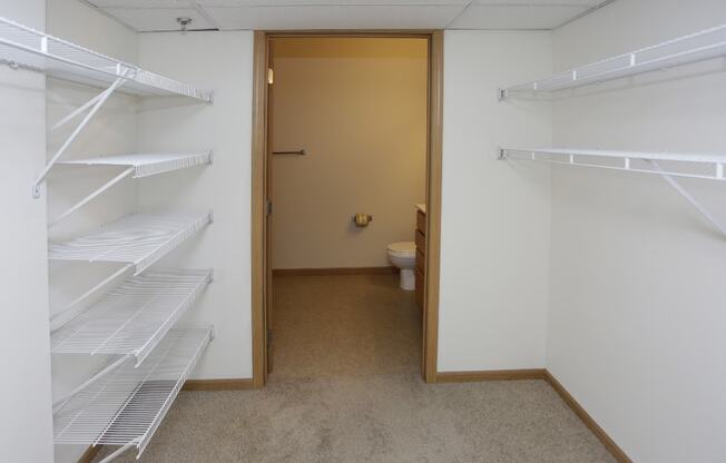 a walk in closet with white shelves and a toilet in the distance