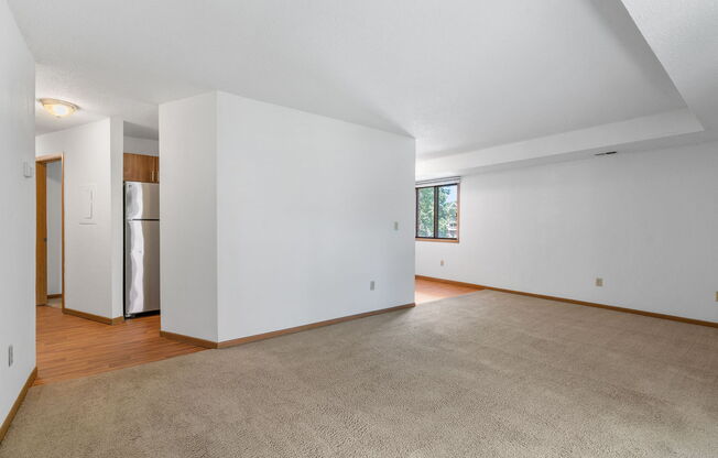 an empty living room with white walls and wood floors and a refrigerator