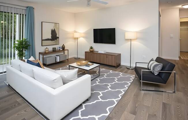 A modern living room with a white sofa, a black armchair, and a television.