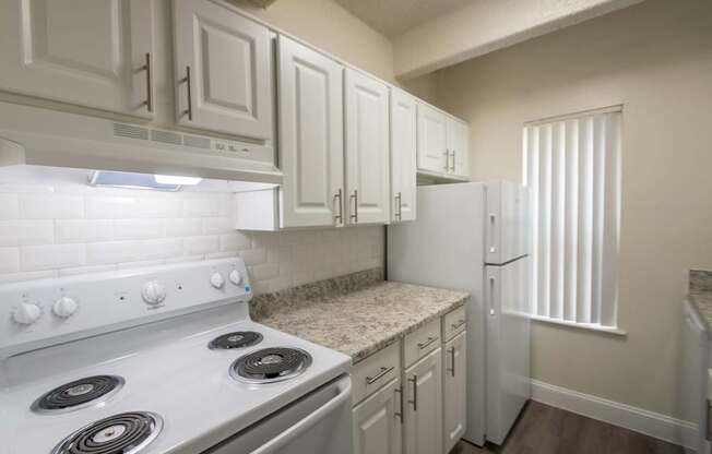 A kitchen with white appliances in a 2 bedroom, 2 bath with balcony apartment home at Harvard Square Apartments in the Vickery Midtown neighborhood of Dallas, TX.