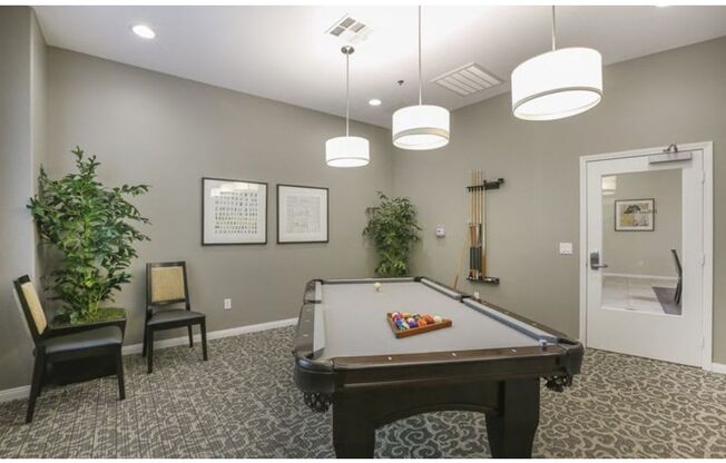 a game room with a pool table and two chairs  at Tesoro Senior Apartments, Porter Ranch, CA