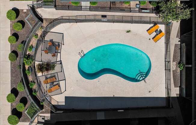 An aerial view of a pool surrounded by a concrete patio and a metal fence.