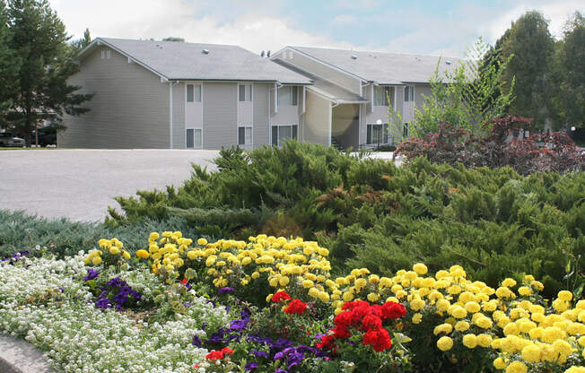 Community landscape with bright yellow, purple, and red flowers, bushes, and apartments behind.at Kirkwood Meadows, Pocatello, 83201