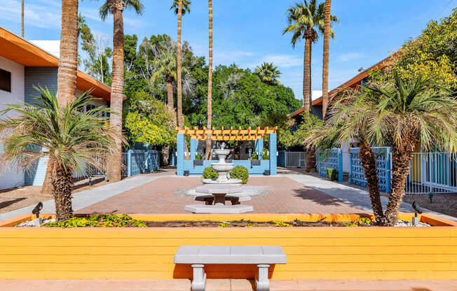 A bright yellow bench sits in front of a blue building with a palm tree at The Phoenix Apartments on 6th Avenue, Phoenix