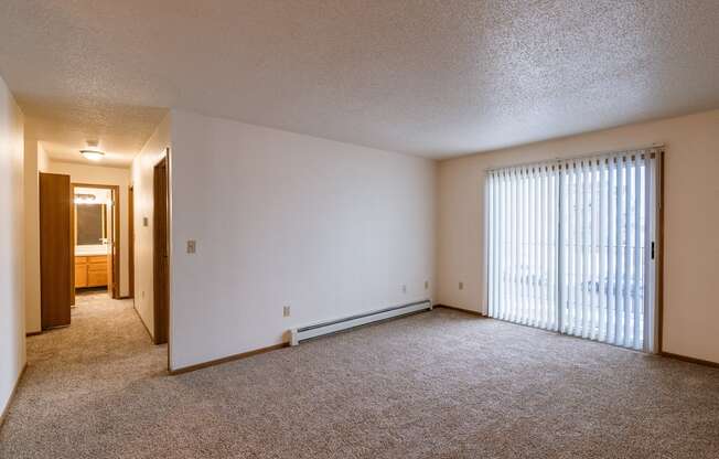 the living room of an apartment with a large window and carpeting. Fargo, ND Country Edge Apartments