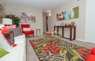 Furnished model living room with a white couch, red chair, and a glass coffee table at Magnolia Apartments in Shreveport, LA