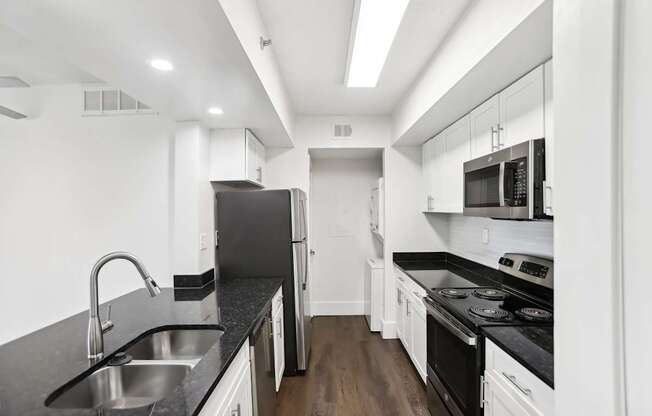 A modern kitchen with stainless steel appliances, black countertops and white cabinets.