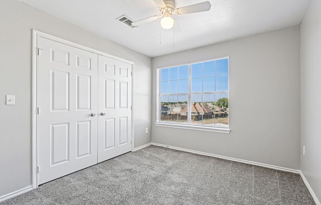 A room with a white door, a ceiling fan, and a window showing a view of houses.