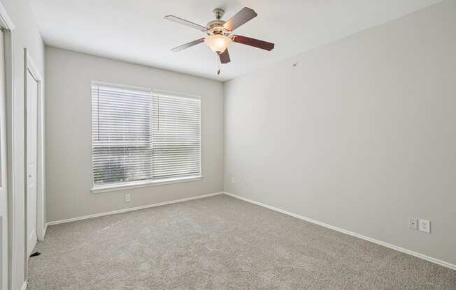 A room with a ceiling fan and a window with blinds.