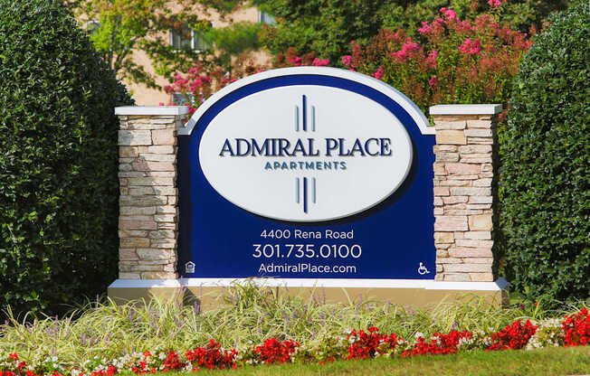 A sign for Admiral Place Apartments is displayed in front of some flowers.