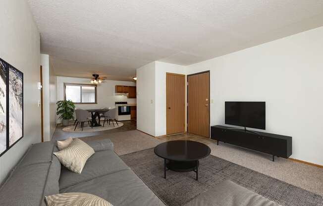 Fargo, ND Gemstone Apartments. A living room with a gray couch and a black coffee table. The dining room is in the background with a 4 chair table.