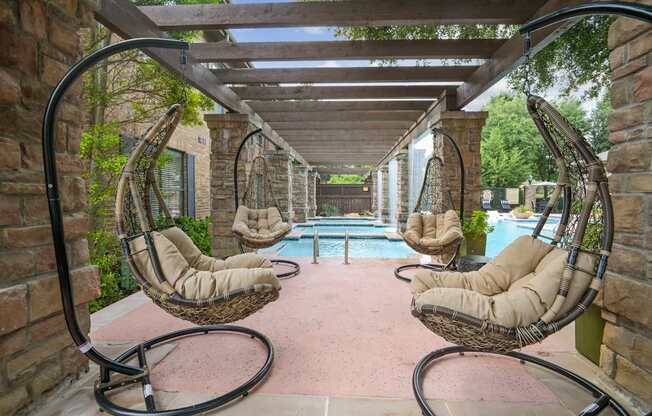 A patio with a pool and hanging chairs.