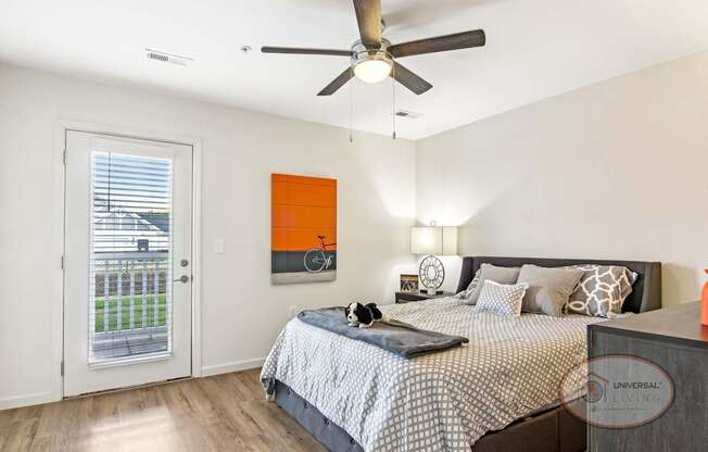 A bedroom with a bed, a ceiling fan, and a glass door leading onto a balcony/patio.