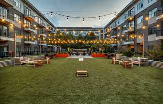 A grassy courtyard surrounded by apartment buildings with string lights hanging above.