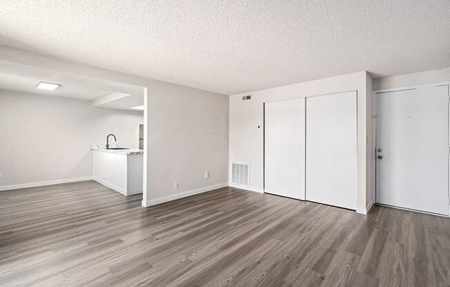 an empty living room with a kitchen in the background