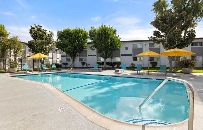 A swimming pool surrounded by trees and chairs with umbrellas.