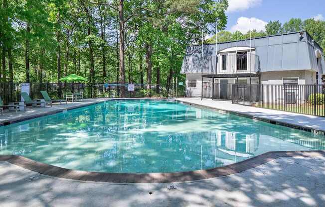 A swimming pool surrounded by trees and a building in the background.