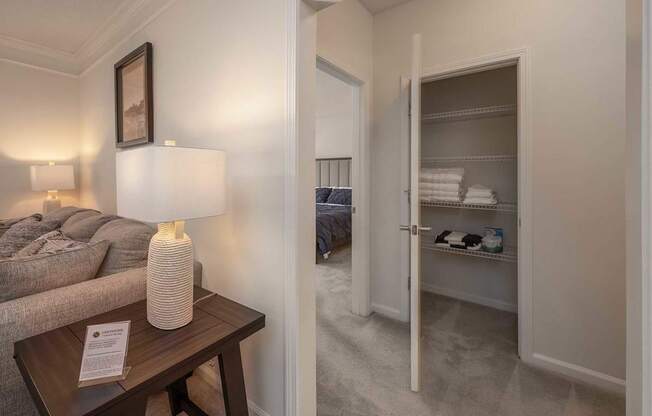 A lamp sits on a table in a room with a bed in the background.