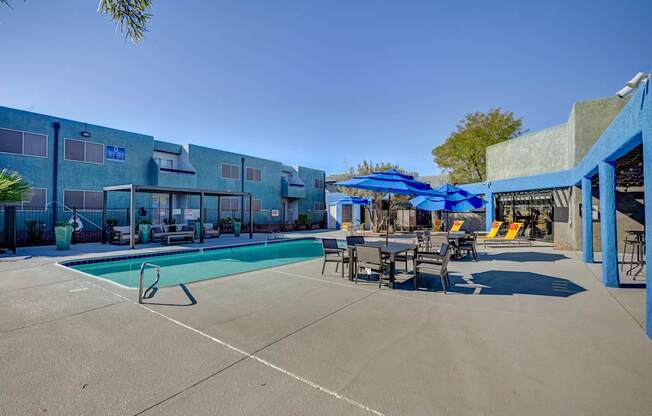 A pool area with a blue umbrella and chairs.