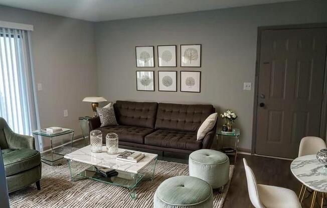 A living room with a brown couch, a glass coffee table, and a grey ottoman.