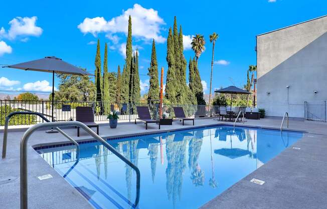 A swimming pool surrounded by trees and chairs.