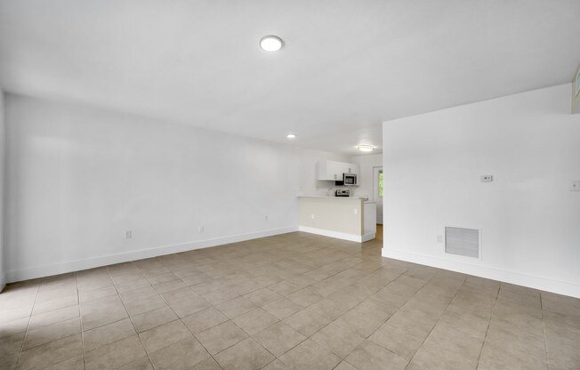 the living room and kitchen of an empty house with white walls and tiled floors