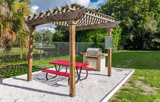 A picnic area with a red table and a wooden pergola.