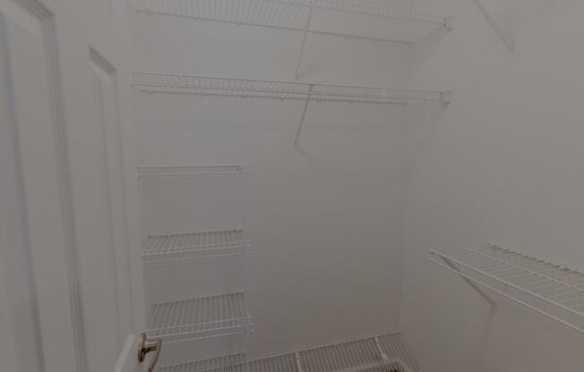 a white walk in closet with white shelves and a white door