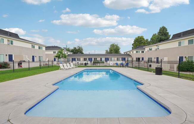 A large outdoor swimming pool surrounded by a fence and chairs.