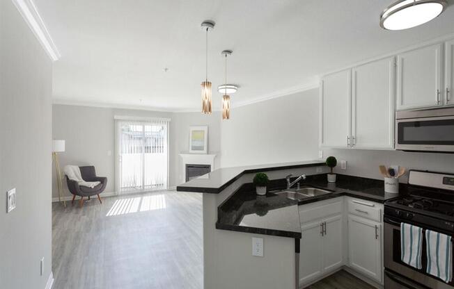 an empty kitchen and living room with white cabinets and black counter tops at Warner Center Townhomes, California, 91303