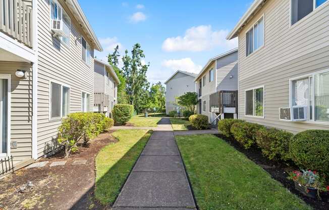 a walkway between two apartment buildings with grass and bushes