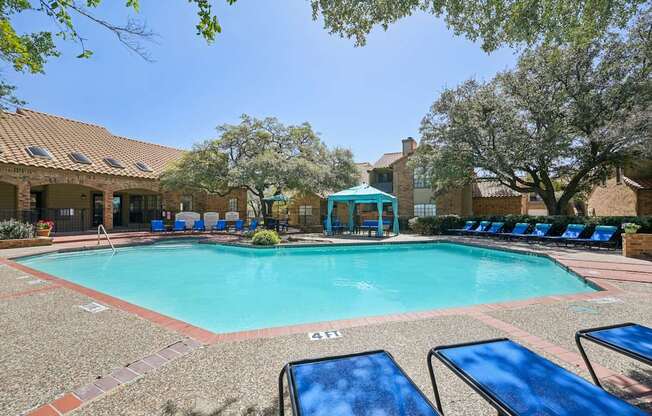 A pool surrounded by sun loungers and trees.