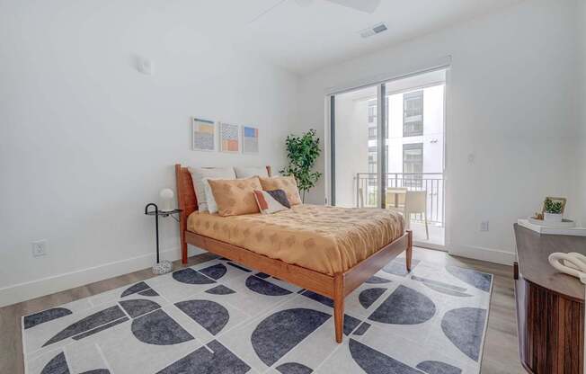 A bedroom with a bed, a rug, and a plant.