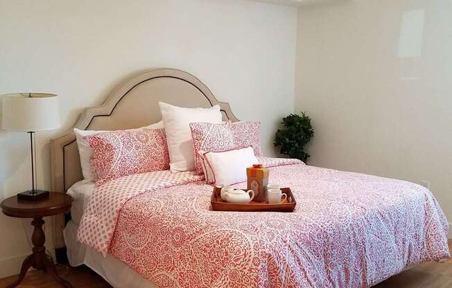 A bed with a red and white patterned comforter and matching pillow cases sits in a room with wooden flooring and white walls at Woodley Sara Apartment, Van Nuys, CA