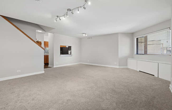 A spacious room with a carpeted floor and a staircase on the left side.